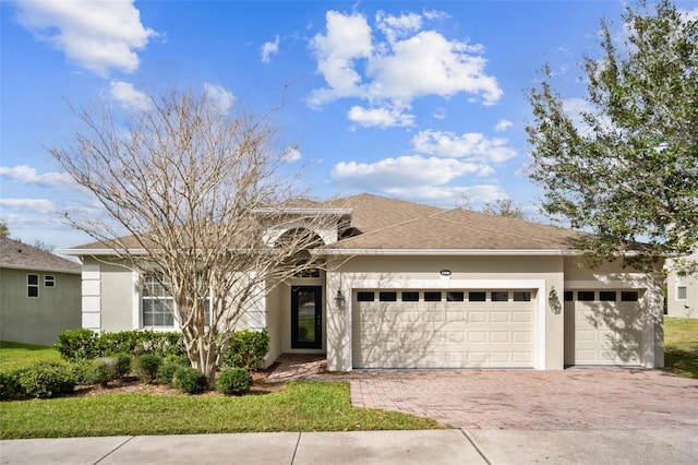 single story home featuring a garage, decorative driveway, a shingled roof, and stucco siding