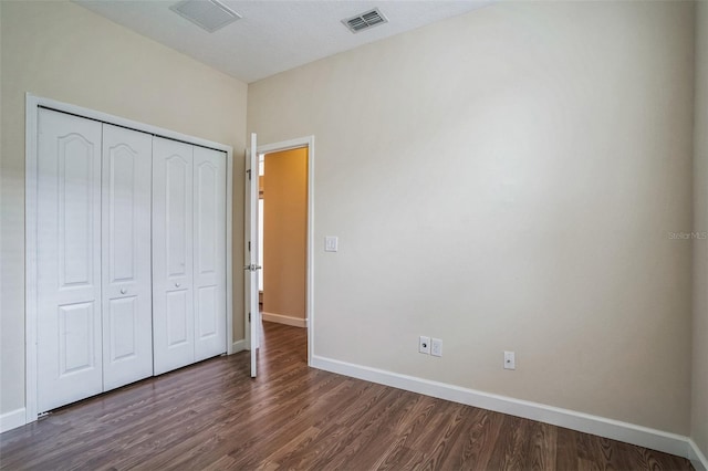 unfurnished bedroom featuring a closet, dark wood-style flooring, visible vents, and baseboards