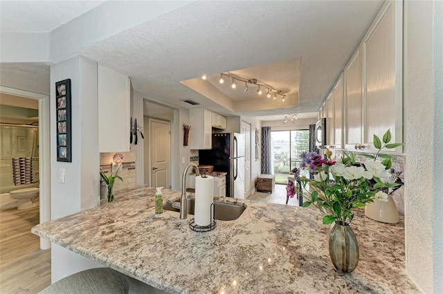 kitchen with light wood finished floors, white cabinets, a peninsula, a textured ceiling, and a sink