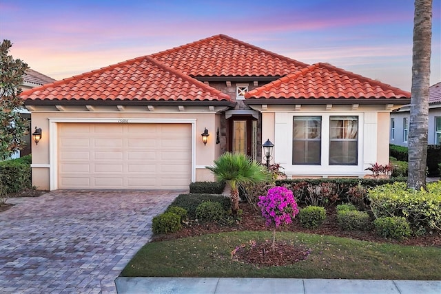 mediterranean / spanish-style house featuring a garage, decorative driveway, a tile roof, and stucco siding