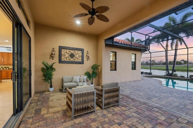 patio terrace at dusk with an outdoor pool, ceiling fan, a water view, a lanai, and an outdoor living space