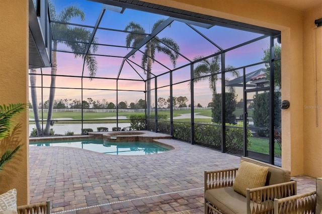 pool at dusk featuring glass enclosure, a patio, a water view, and a pool with connected hot tub