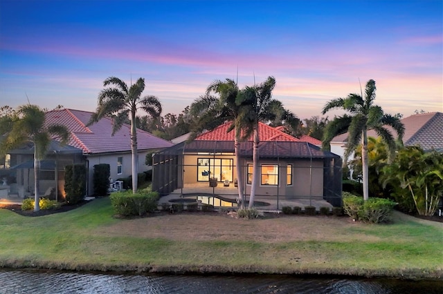 rear view of property featuring a tiled roof, a lawn, a lanai, and stucco siding