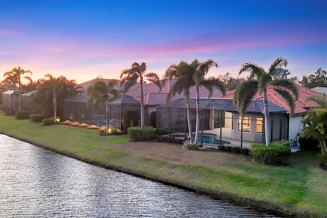 back of property featuring a lanai, a water view, an outdoor pool, and a lawn