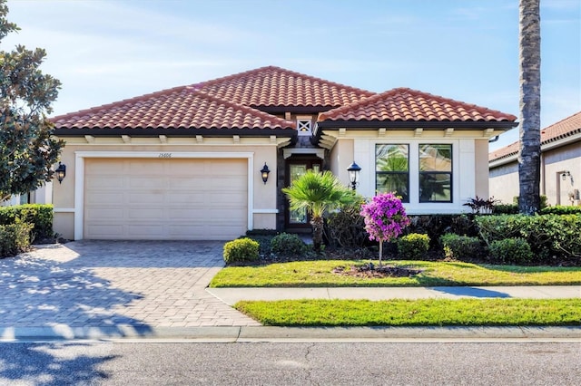 mediterranean / spanish house with an attached garage, a tiled roof, decorative driveway, and stucco siding