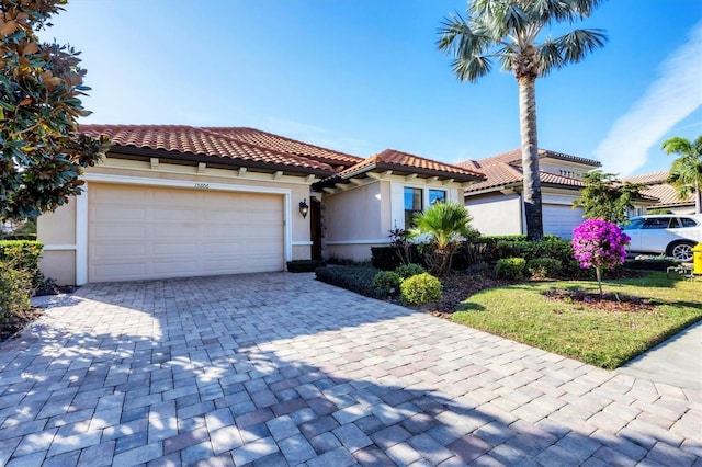 mediterranean / spanish house featuring a tiled roof, decorative driveway, an attached garage, and stucco siding