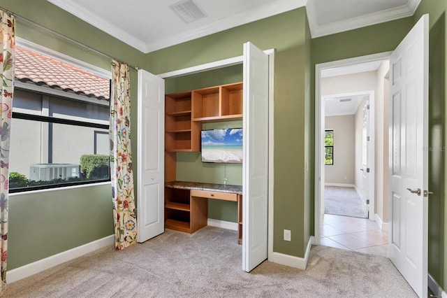 unfurnished bedroom featuring crown molding, baseboards, built in study area, and light colored carpet