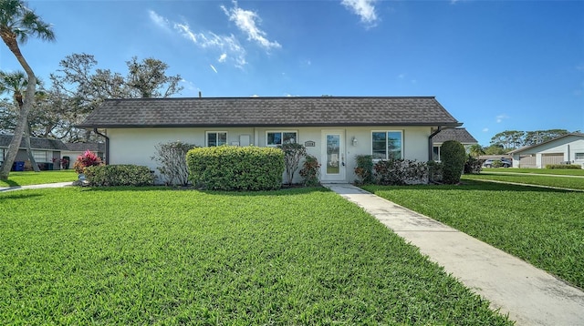 ranch-style house with stucco siding, a front yard, mansard roof, and roof with shingles