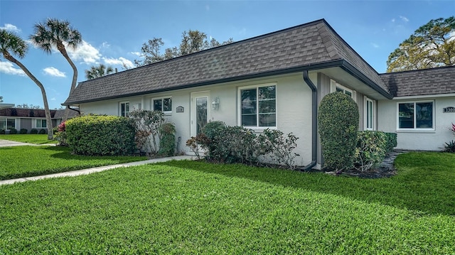 view of front of home featuring stucco siding, a front yard, mansard roof, and roof with shingles