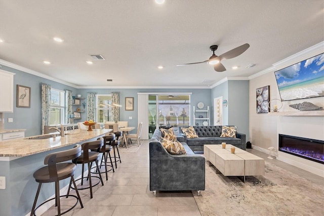 living area featuring a glass covered fireplace, light tile patterned flooring, crown molding, and baseboards