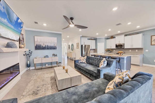 living area featuring baseboards, visible vents, a glass covered fireplace, ornamental molding, and recessed lighting