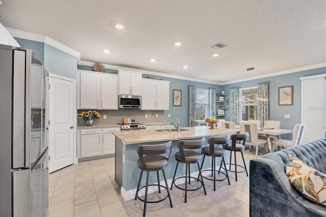 kitchen featuring light stone counters, a center island with sink, decorative backsplash, appliances with stainless steel finishes, and white cabinets