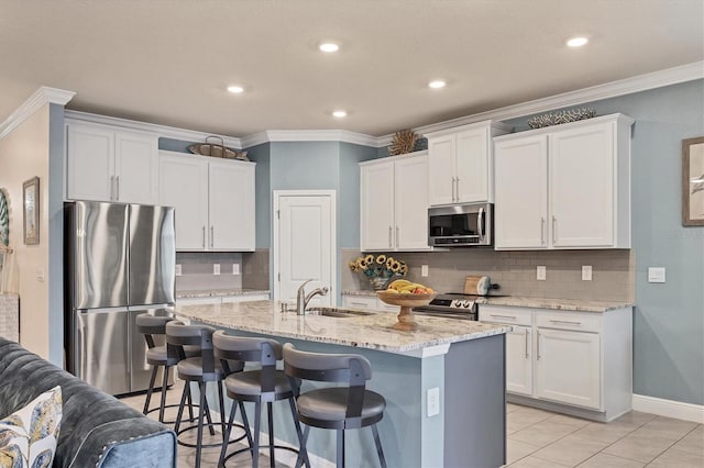 kitchen with a center island with sink, light stone countertops, stainless steel appliances, white cabinetry, and a sink