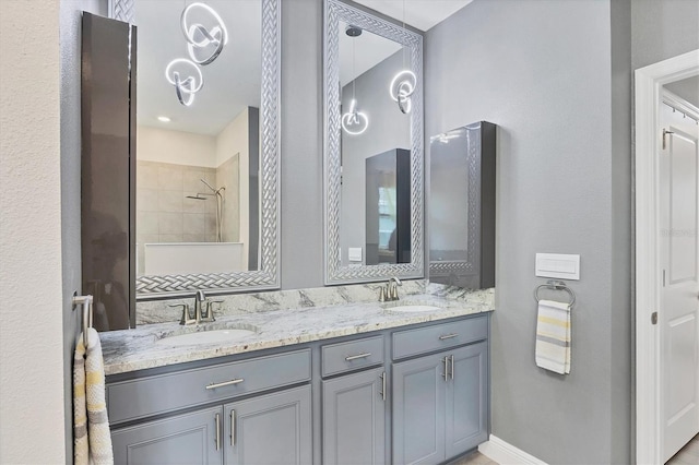 full bathroom with double vanity, tiled shower, a sink, and baseboards