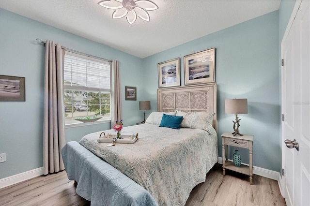 bedroom featuring baseboards, a textured ceiling, and light wood finished floors