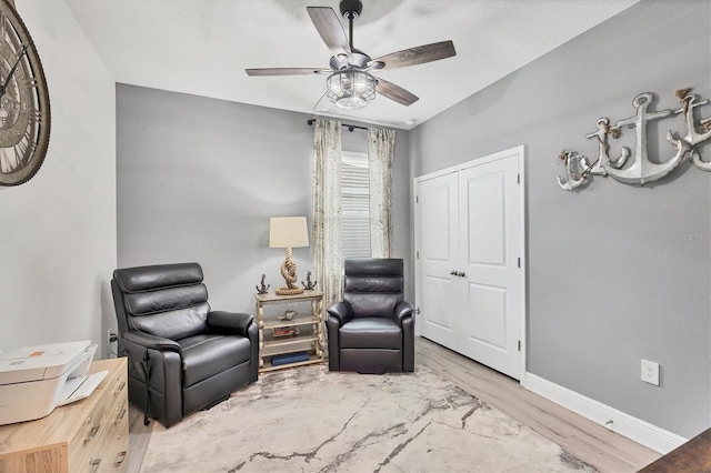 living area with wood finished floors, a ceiling fan, and baseboards