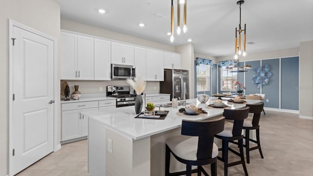 kitchen featuring decorative light fixtures, a center island with sink, stainless steel appliances, light countertops, and white cabinets