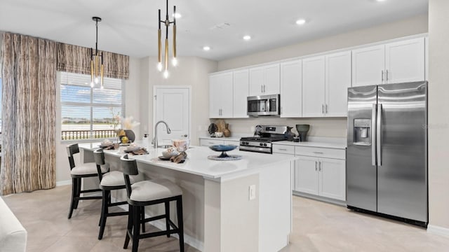 kitchen with stainless steel appliances, white cabinetry, hanging light fixtures, light countertops, and an island with sink