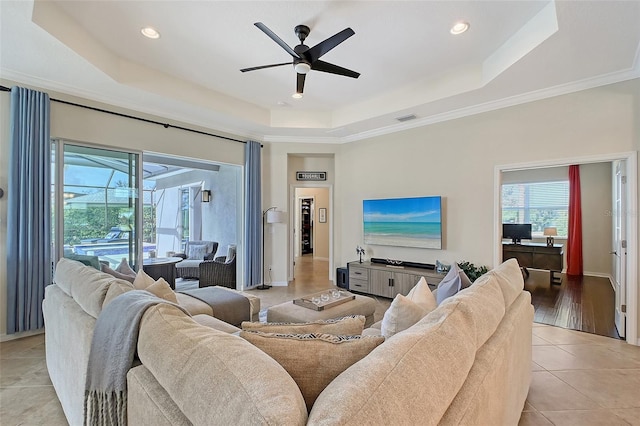 living room featuring light tile patterned floors, visible vents, baseboards, a ceiling fan, and a tray ceiling