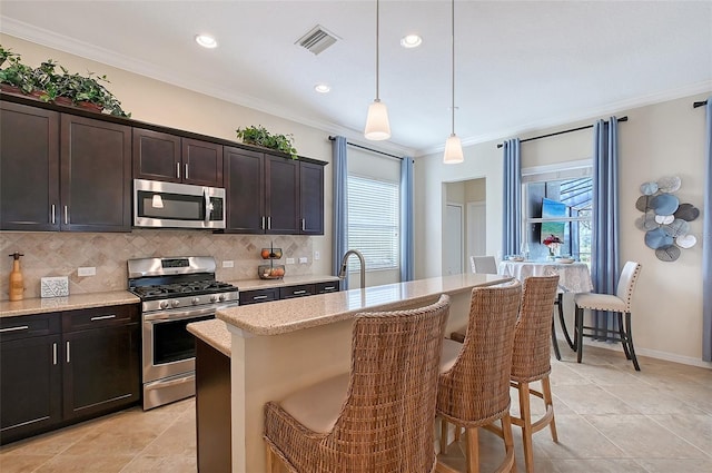 kitchen featuring decorative light fixtures, stainless steel appliances, ornamental molding, a kitchen island with sink, and a kitchen bar