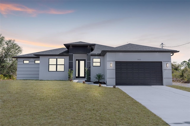 prairie-style home featuring a yard, an attached garage, and stucco siding