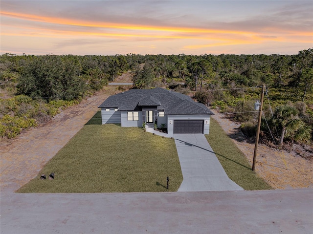 view of front of home featuring an attached garage, a forest view, concrete driveway, and a yard