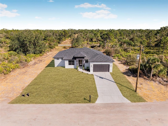 view of front of property featuring concrete driveway, a front lawn, a forest view, and an attached garage