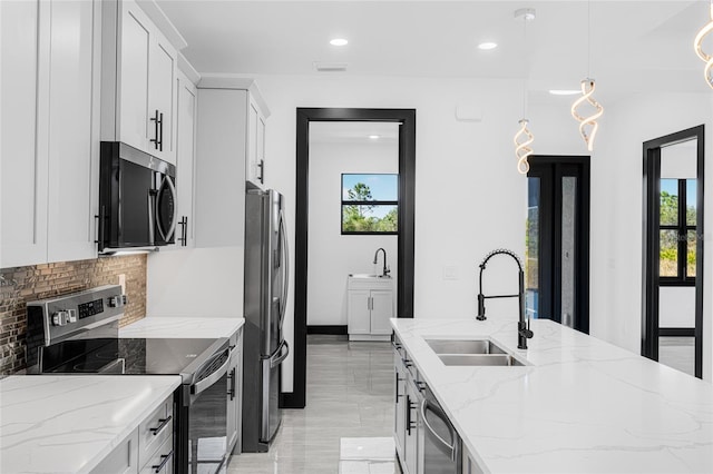 kitchen with light stone counters, stainless steel appliances, a sink, white cabinets, and decorative light fixtures