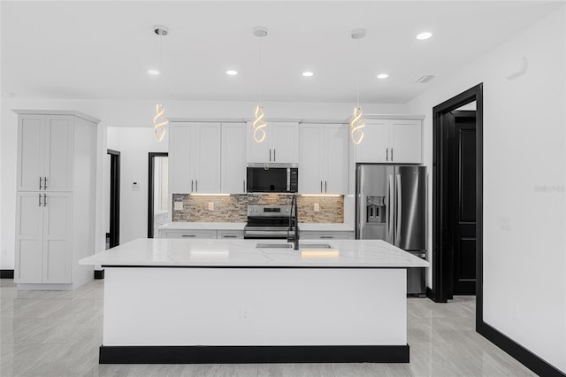 kitchen with a kitchen island with sink, white cabinets, appliances with stainless steel finishes, light stone countertops, and decorative light fixtures