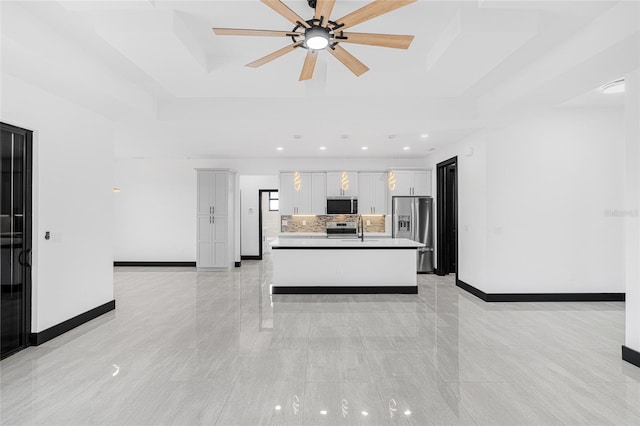 kitchen with pendant lighting, stainless steel appliances, a raised ceiling, white cabinetry, and an island with sink