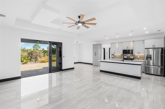 kitchen with appliances with stainless steel finishes, a raised ceiling, hanging light fixtures, and an island with sink