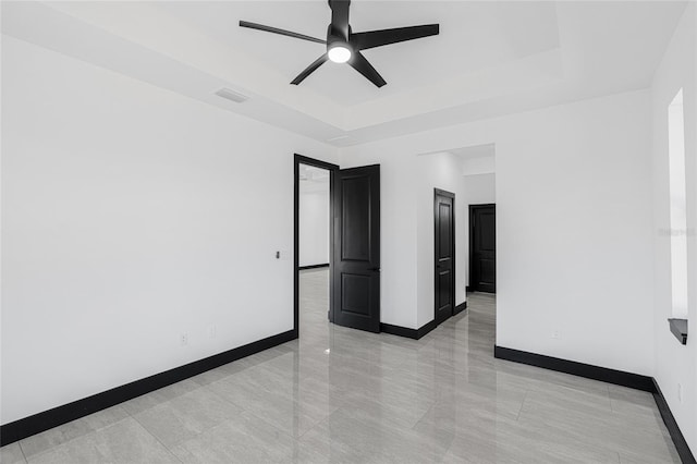 unfurnished room with ceiling fan, visible vents, baseboards, and a raised ceiling