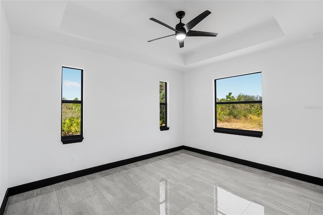 unfurnished room featuring a raised ceiling, a ceiling fan, and baseboards