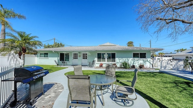 rear view of property featuring a patio area, fence, a lawn, and stucco siding