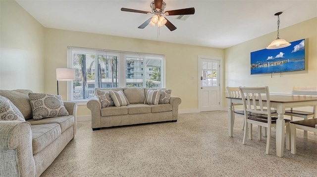 living area with light speckled floor, a ceiling fan, and baseboards