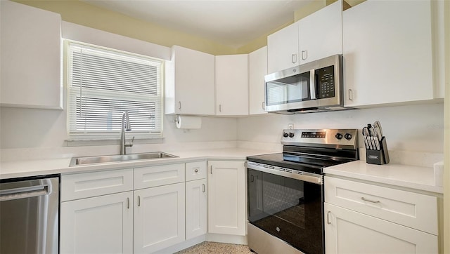 kitchen with light countertops, appliances with stainless steel finishes, a sink, and white cabinetry
