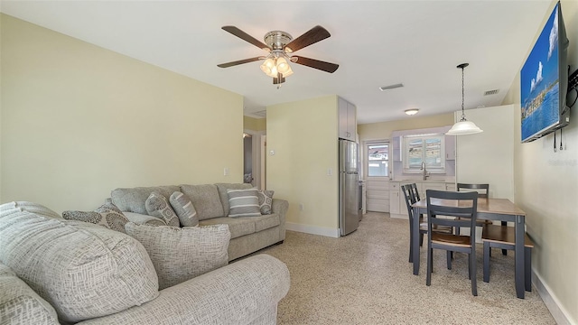 living area featuring light speckled floor, a ceiling fan, visible vents, and baseboards