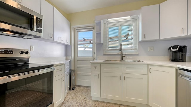 kitchen featuring light speckled floor, stainless steel appliances, a sink, white cabinets, and light countertops