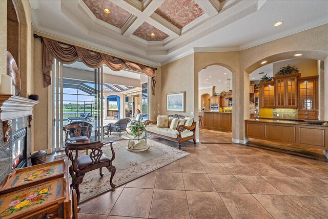 sitting room featuring crown molding, light tile patterned floors, a high ceiling, a premium fireplace, and coffered ceiling