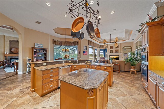 kitchen with open floor plan, a kitchen island with sink, a raised ceiling, and a lit fireplace