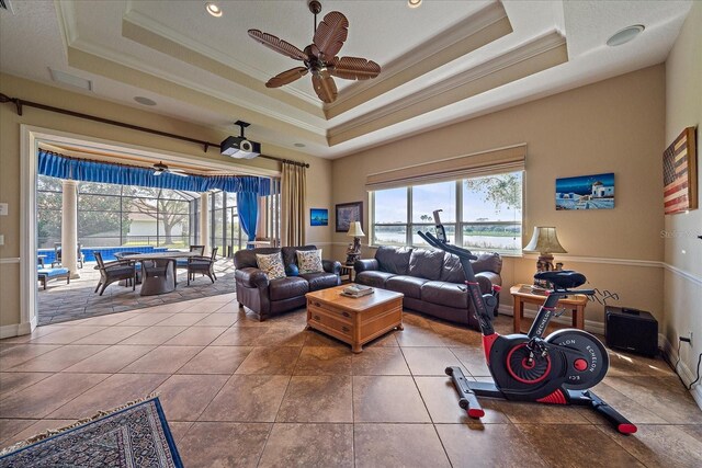 living room with a ceiling fan, baseboards, ornamental molding, tile patterned floors, and a raised ceiling