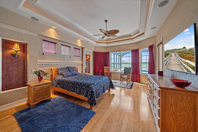 bedroom featuring light wood-type flooring, a tray ceiling, and ornamental molding