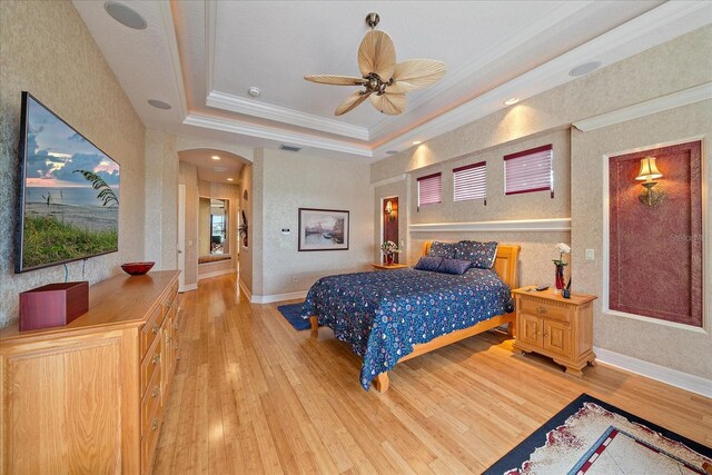 bedroom featuring arched walkways, a tray ceiling, ornamental molding, and light wood-style floors