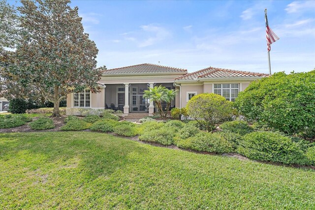 back of house featuring a sunroom, a lawn, and stucco siding