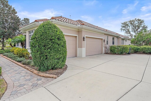 view of side of property with a tile roof, driveway, an attached garage, and stucco siding