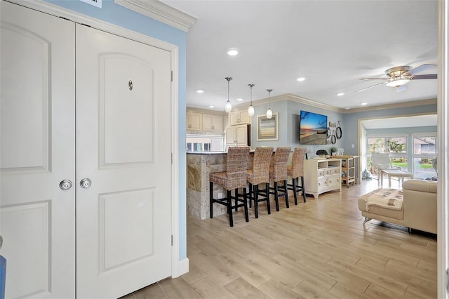 kitchen with ceiling fan, ornamental molding, light wood finished floors, a kitchen bar, and decorative light fixtures