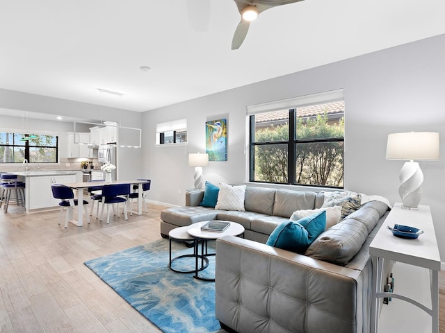 living area with baseboards, a ceiling fan, and light wood-style floors