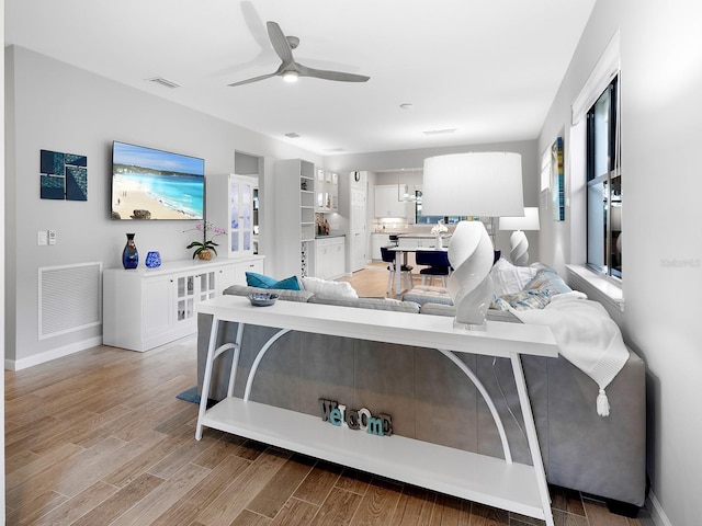 living room with a ceiling fan, baseboards, visible vents, and light wood finished floors