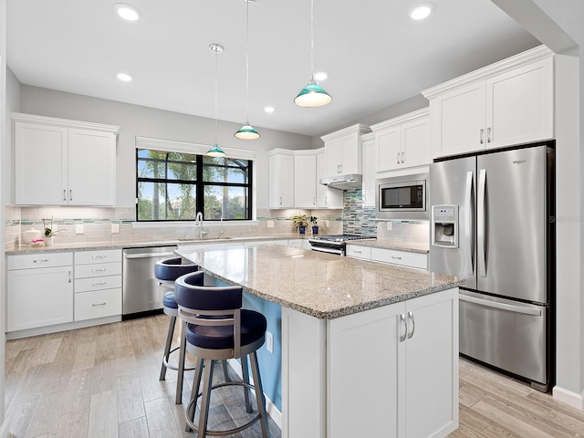 kitchen featuring a center island, stainless steel appliances, white cabinetry, a sink, and under cabinet range hood