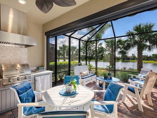 view of patio featuring an outdoor kitchen, a ceiling fan, area for grilling, glass enclosure, and a water view